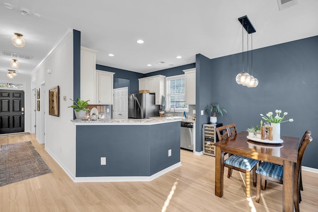 kitchen featuring pendant lighting, white cabinetry, stainless steel appliances, tasteful backsplash, and light hardwood / wood-style flooring