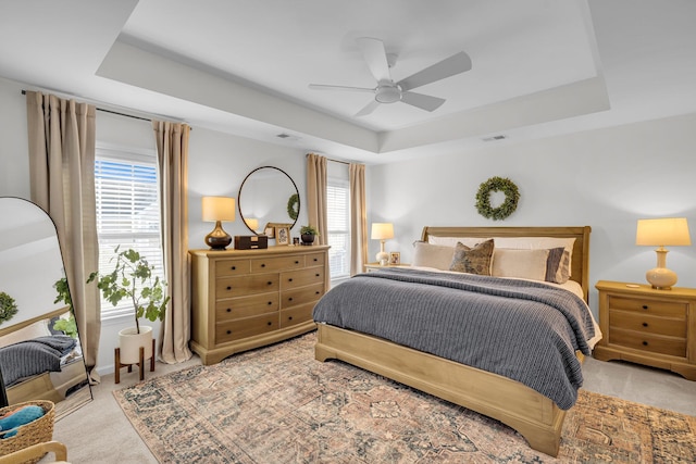 bedroom featuring a raised ceiling, light colored carpet, and ceiling fan