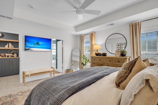 carpeted bedroom with ceiling fan, a raised ceiling, and multiple windows