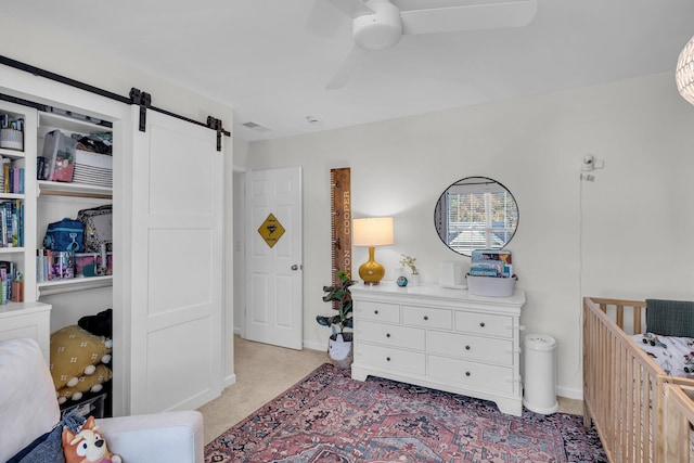 bedroom featuring light carpet, ceiling fan, a barn door, and a nursery area