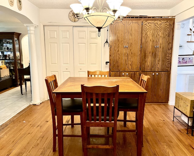 dining space with light hardwood / wood-style floors, a textured ceiling, and an inviting chandelier