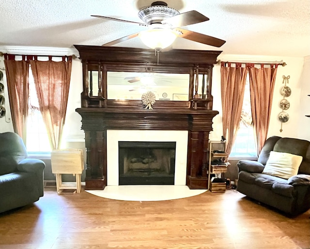 sitting room with hardwood / wood-style floors, ceiling fan, a large fireplace, and a textured ceiling