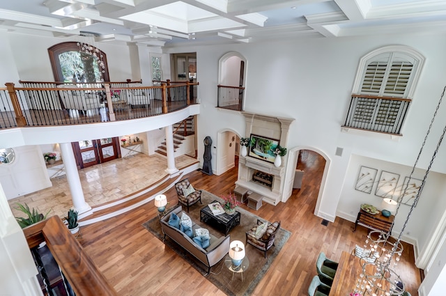 living room featuring coffered ceiling, light hardwood / wood-style flooring, beam ceiling, a towering ceiling, and ornate columns