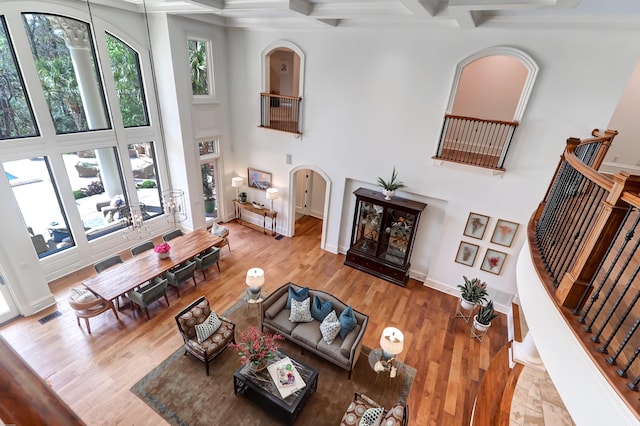 living room with a towering ceiling, beam ceiling, coffered ceiling, and light hardwood / wood-style floors