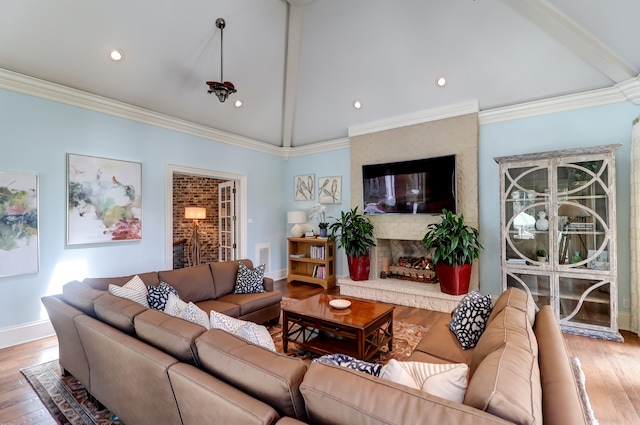 living room with lofted ceiling with beams, light hardwood / wood-style floors, crown molding, and a fireplace