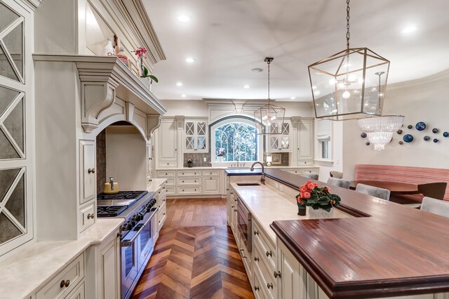 kitchen with wood counters, dark parquet flooring, a center island with sink, appliances with stainless steel finishes, and hanging light fixtures