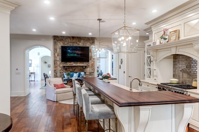 kitchen featuring butcher block counters, decorative light fixtures, a fireplace, dark wood-type flooring, and a kitchen bar