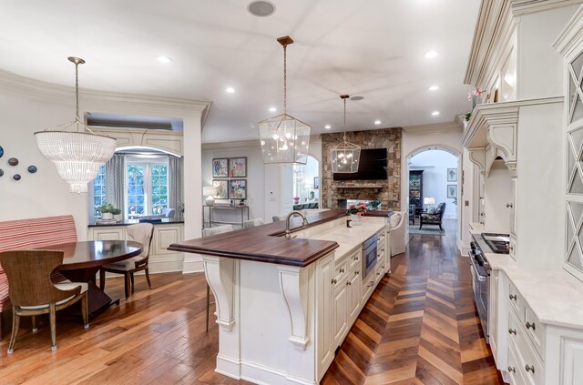 kitchen with decorative light fixtures, a notable chandelier, an island with sink, a stone fireplace, and crown molding