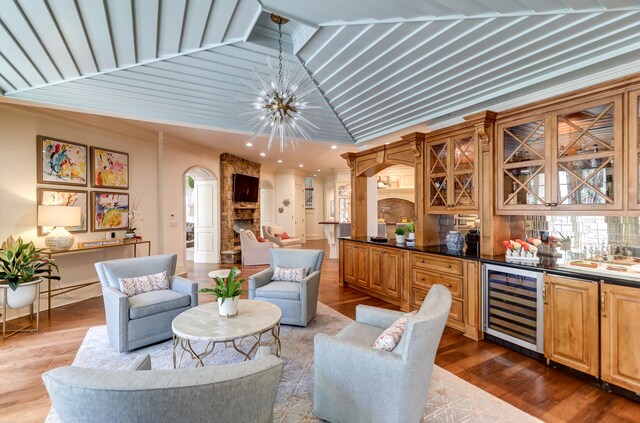 sitting room with crown molding, hardwood / wood-style floors, a fireplace, beverage cooler, and an inviting chandelier