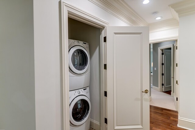 laundry room with stacked washer / drying machine, dark wood-type flooring, and crown molding