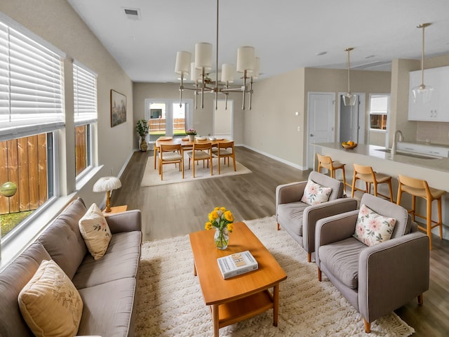 living room with visible vents, baseboards, an inviting chandelier, and wood finished floors