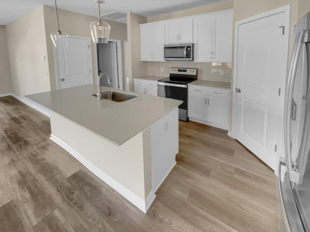 kitchen featuring an island with sink, a sink, appliances with stainless steel finishes, white cabinetry, and light wood-type flooring