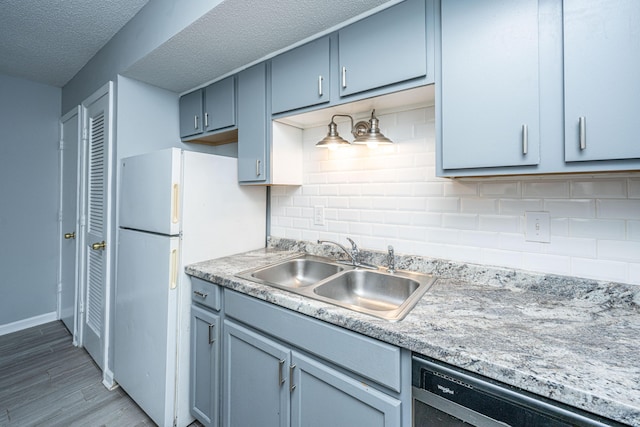 kitchen with sink, dishwashing machine, backsplash, white refrigerator, and light hardwood / wood-style flooring