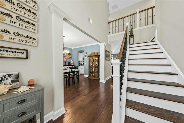 staircase with crown molding, wood-type flooring, decorative columns, and a notable chandelier