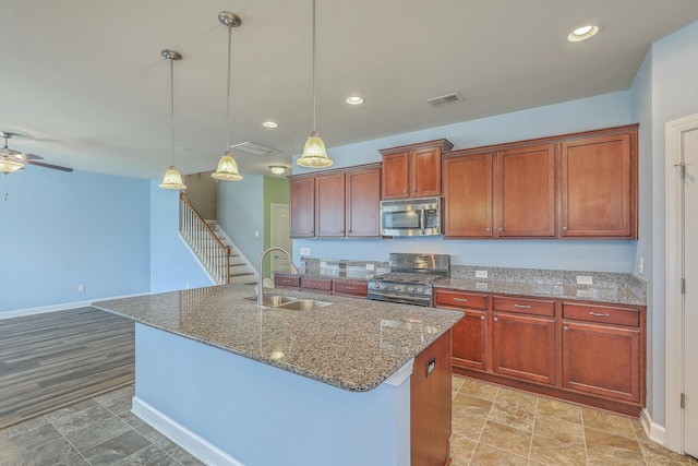 kitchen featuring an island with sink, pendant lighting, stainless steel appliances, and a sink