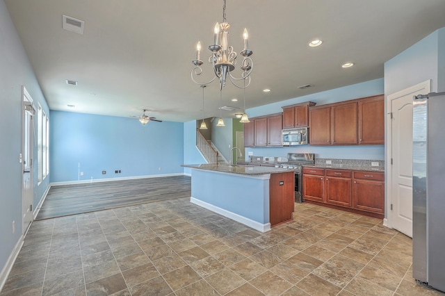 kitchen with stainless steel appliances, hanging light fixtures, brown cabinetry, open floor plan, and an island with sink