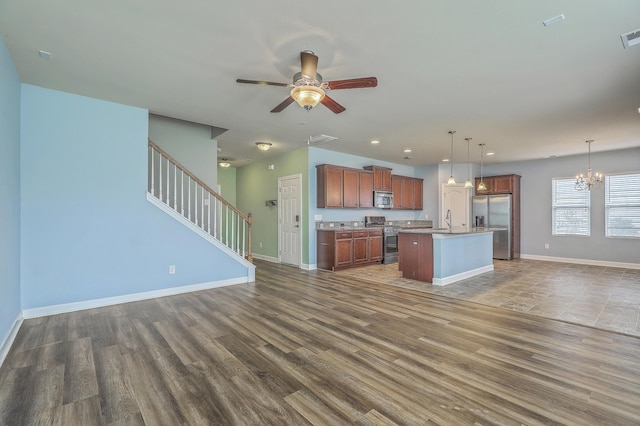 kitchen with stainless steel appliances, a sink, open floor plan, hanging light fixtures, and an island with sink