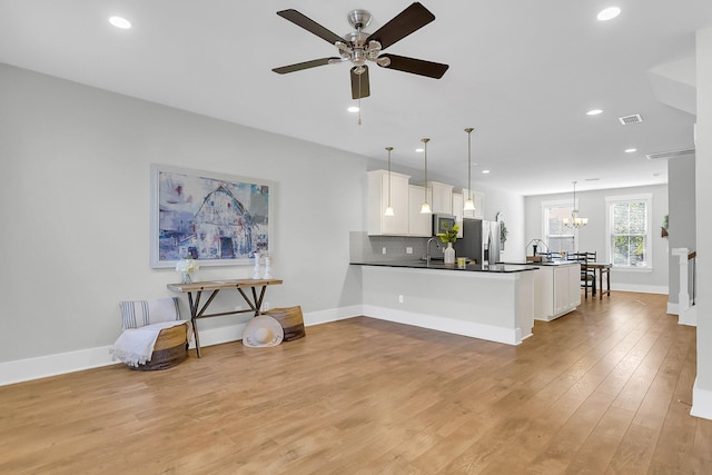 kitchen with pendant lighting, appliances with stainless steel finishes, white cabinetry, light hardwood / wood-style floors, and kitchen peninsula