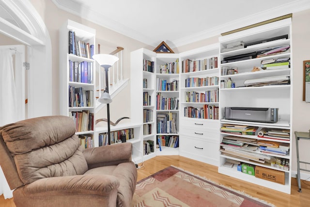 living area with light wood-style flooring, crown molding, and wall of books