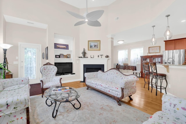 living area with a fireplace, light wood-style floors, visible vents, and ceiling fan