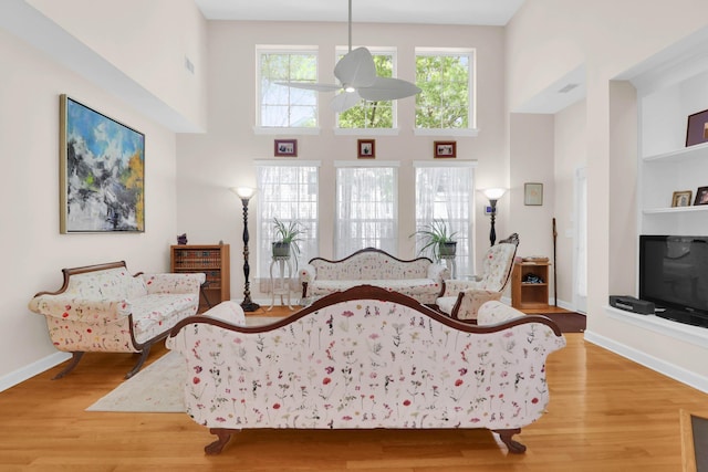 living room with light wood-style flooring, a ceiling fan, a high ceiling, and baseboards