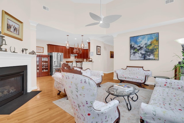 living room with light wood finished floors, visible vents, baseboards, and ceiling fan