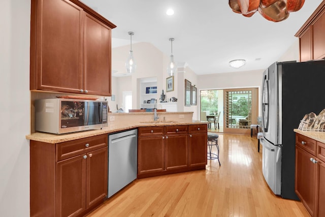 kitchen featuring a peninsula, vaulted ceiling, appliances with stainless steel finishes, a sink, and light wood finished floors