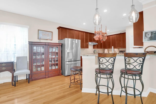 kitchen featuring stainless steel fridge, light wood-style flooring, under cabinet range hood, a kitchen bar, and hanging light fixtures