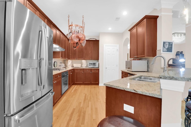 kitchen featuring a peninsula, under cabinet range hood, light stone countertops, stainless steel appliances, and a sink