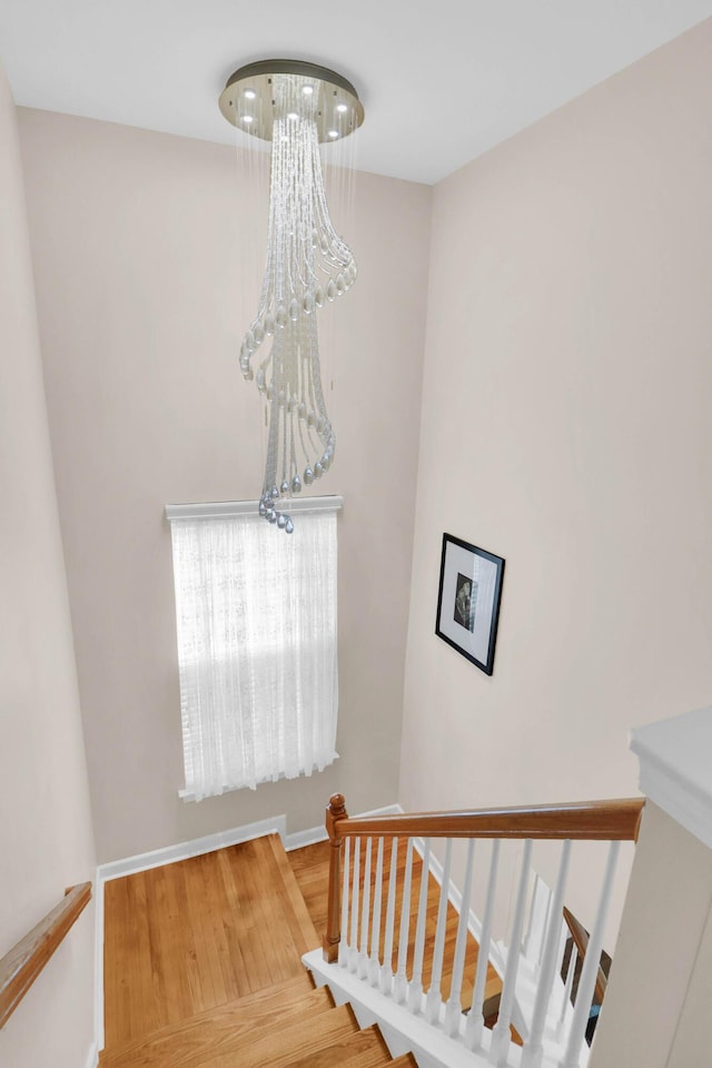 stairway with baseboards, an inviting chandelier, and wood finished floors