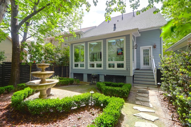 back of house with a sunroom, roof with shingles, and fence