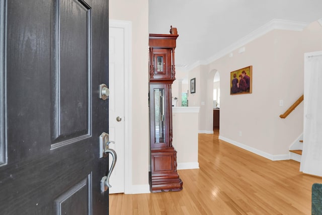 entrance foyer featuring baseboards, ornamental molding, stairway, light wood-style flooring, and arched walkways