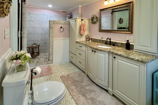 bathroom with a walk in shower, crown molding, vanity, toilet, and a wainscoted wall