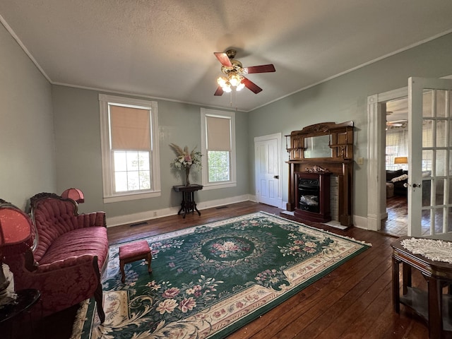 living area with a ceiling fan, wood-type flooring, a fireplace with flush hearth, ornamental molding, and baseboards