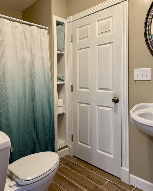 bathroom featuring toilet, wood finished floors, and curtained shower