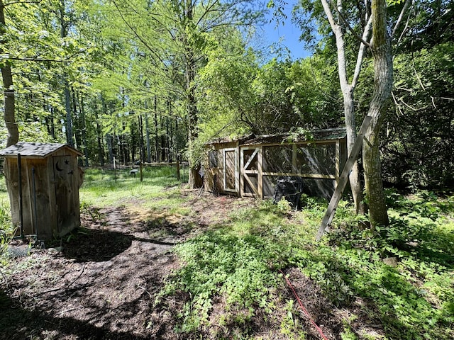 view of yard with an outdoor structure, a view of trees, and a storage shed