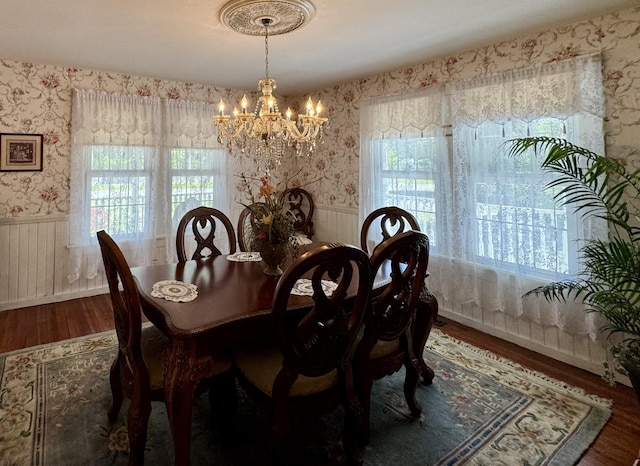 dining room featuring a chandelier, wood finished floors, wallpapered walls, wainscoting, and healthy amount of natural light