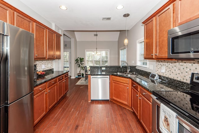 kitchen with dark stone countertops, hanging light fixtures, stainless steel appliances, and a notable chandelier