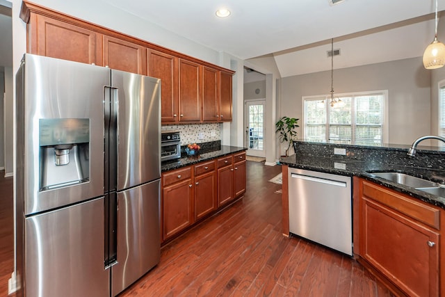 kitchen featuring appliances with stainless steel finishes, dark stone counters, sink, a notable chandelier, and hanging light fixtures