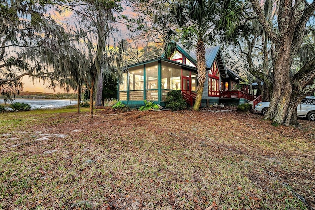 yard at dusk with a water view and a sunroom