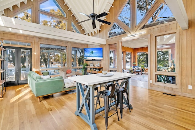 dining area featuring light wood-type flooring, high vaulted ceiling, ceiling fan, and wooden walls