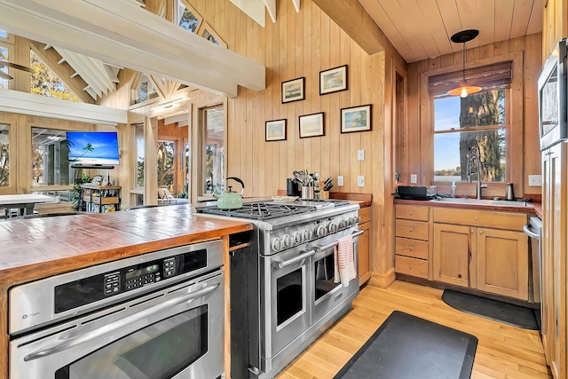 kitchen with decorative light fixtures, stainless steel appliances, light hardwood / wood-style flooring, and wooden walls