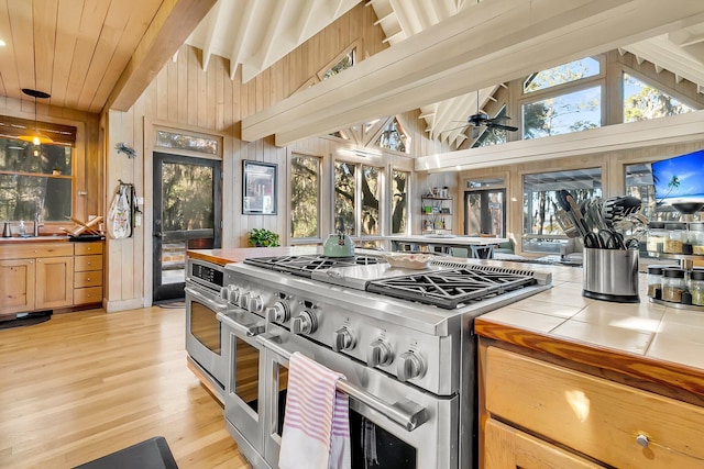 kitchen featuring appliances with stainless steel finishes, ceiling fan, decorative light fixtures, tile counters, and wood walls