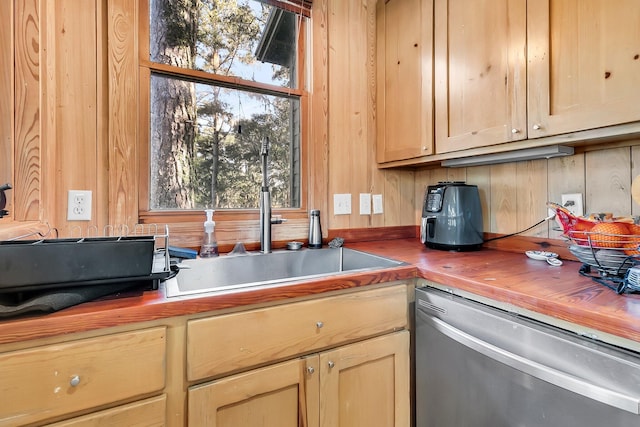 kitchen featuring wooden walls, dishwasher, sink, and light brown cabinetry