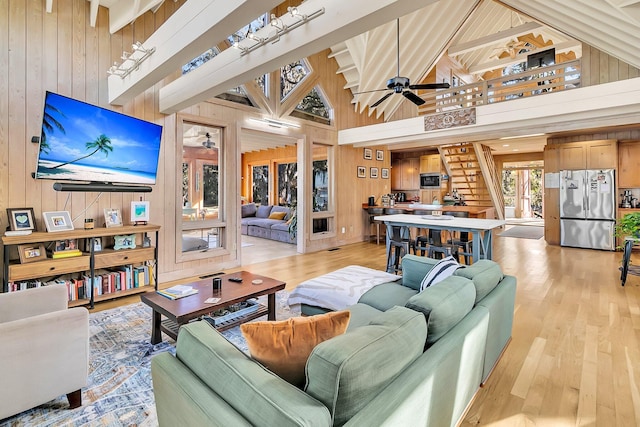 living room with ceiling fan, wood walls, light hardwood / wood-style floors, and high vaulted ceiling