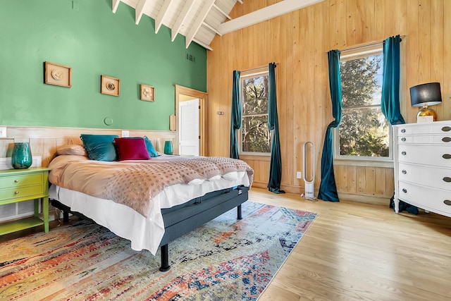 bedroom with light wood-type flooring, wood ceiling, beam ceiling, high vaulted ceiling, and wood walls