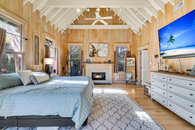 bedroom featuring beamed ceiling, light hardwood / wood-style flooring, high vaulted ceiling, and wood walls