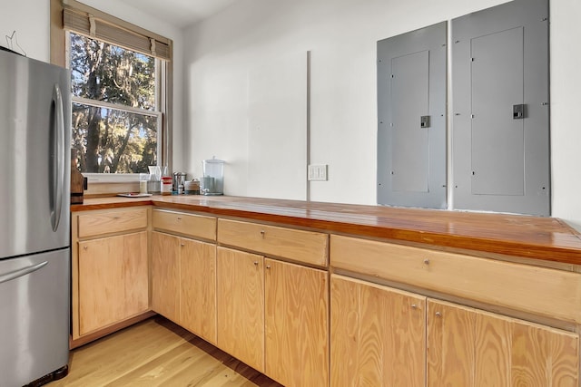 kitchen featuring light brown cabinets, electric panel, wooden counters, light hardwood / wood-style flooring, and stainless steel fridge