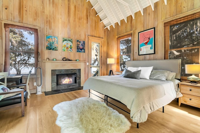 bedroom featuring lofted ceiling with beams, light hardwood / wood-style floors, a tiled fireplace, and multiple windows