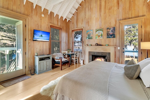 bedroom with access to exterior, wood ceiling, hardwood / wood-style floors, vaulted ceiling with beams, and a tiled fireplace